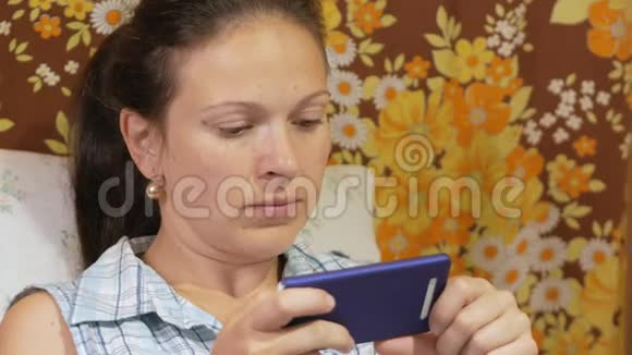 一个年轻的女人正在家里的沙发上用手机查看信息视频的预览图