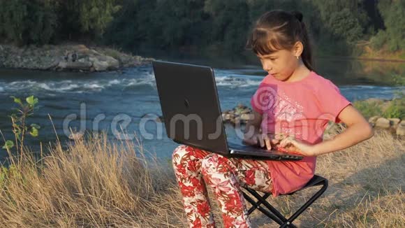 河岸上的女孩带着笔记本电脑一个小女孩拿着笔记本电脑在一条小河的岸边视频的预览图
