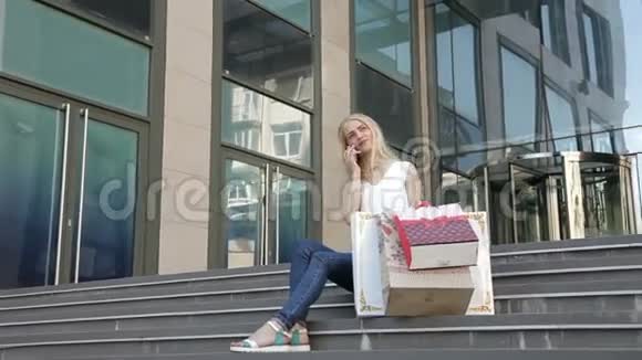 年轻女孩拿着购物袋坐在台阶上打着电话视频的预览图