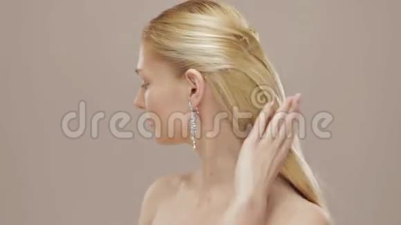 漂亮的金发女孩抚摸着她的头发转向照相机视频的预览图