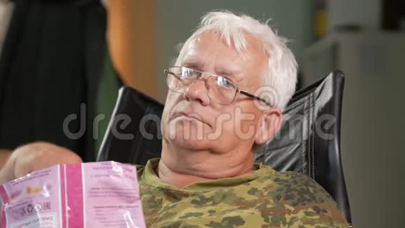 老人吃玉米棒看电视坐在带眼镜的皮扶手椅上视频的预览图