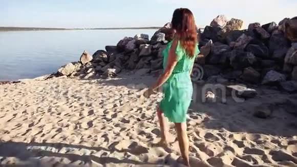 一个穿绿色连衣裙的漂亮女孩正沿着海岸散步视频的预览图