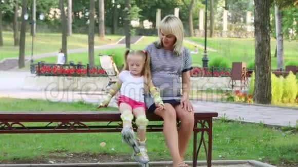 在阳光公园孕妇和穿着旱冰鞋的小女孩坐在长凳上视频的预览图