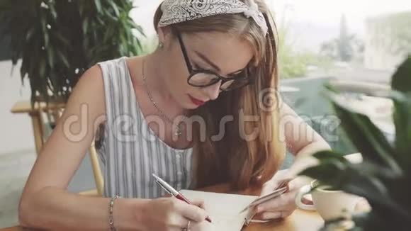 年轻女子从卡片到笔记本写信息女作家在咖啡馆写作视频的预览图