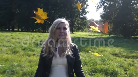 美丽的金发女人在公园扔黄色留下正能量秋天的背景视频的预览图