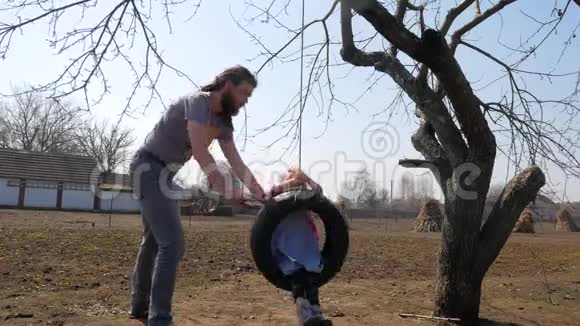 父亲一边在公园里玩一边把女儿推到秋千上视频的预览图