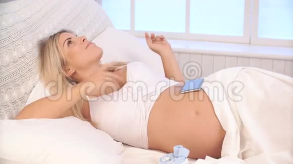躺在床上用智能手机听音乐的孕妇视频的预览图
