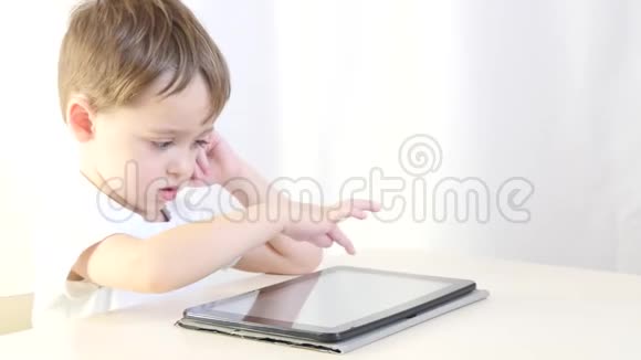 快乐的孩子坐在桌子旁玩平板电脑孩子在玩电子游戏因特网和无线视频的预览图