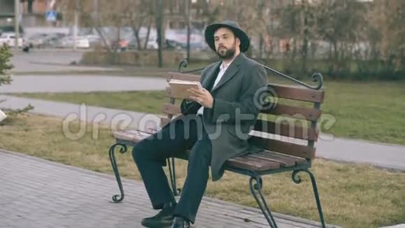在公园里坐在城市街头的长椅上一个戴着帽子穿着外套拿着笔和素描的艺术家视频的预览图