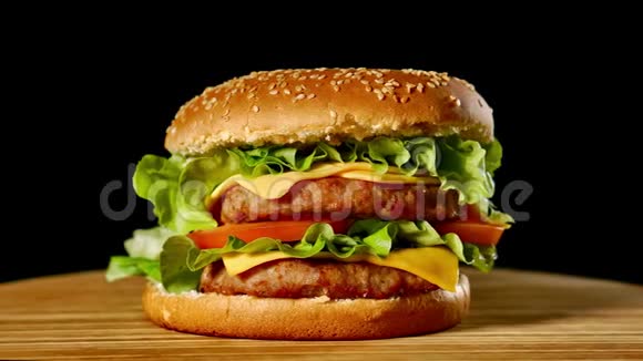大汉堡配牛肉西红柿蘑菇和黄瓜配上融化的奶酪在黑色的木板上旋转视频的预览图