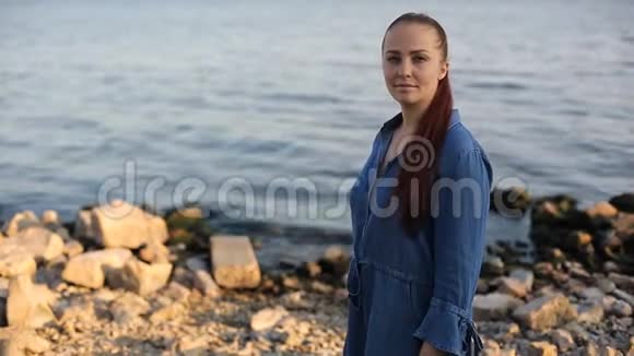 年轻美丽的白人中年妇女红色头发穿着蓝色牛仔裙站在海边视频的预览图