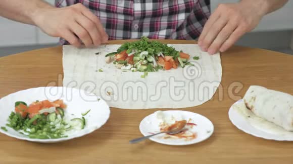 男人正在家里的餐桌上做饭皮塔蔬菜和葱配酱汁和蛋黄酱关闭视频的预览图