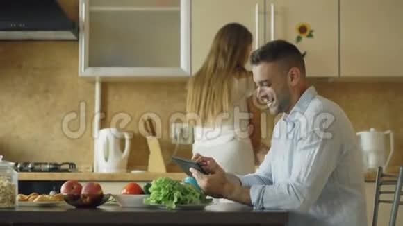 一对漂亮的夫妇一大早就在厨房里聊天美丽的女人一边做饭一边喂丈夫视频的预览图