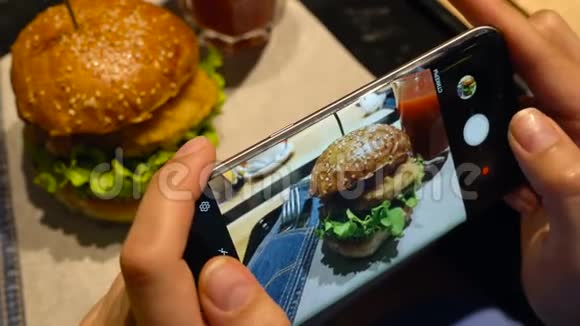 女孩在一家咖啡馆里的智能手机上拍了一张汉堡和番茄汁的照片视频的预览图