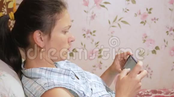 一个年轻的女人正在家里的沙发上用手机查看信息视频的预览图