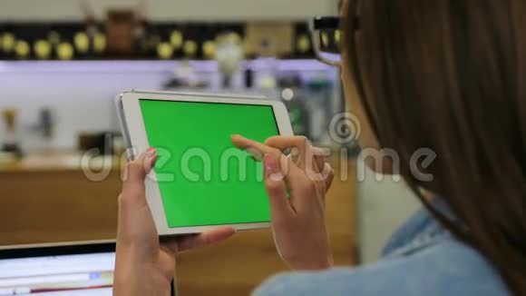 年轻漂亮的女人用平板电脑和绿色屏幕坐在咖啡馆里滑动图片特写镜头铬键视频的预览图