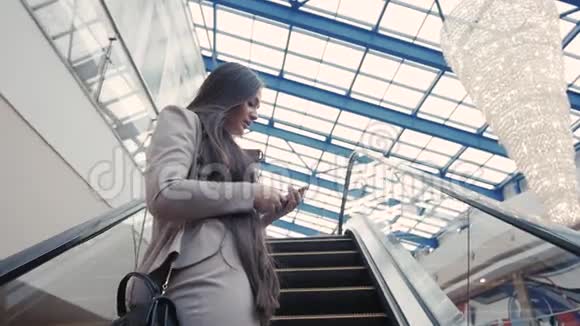 自信的女人正在通过手机上网看电子邮件而站在自动扶梯的购物中心视频的预览图