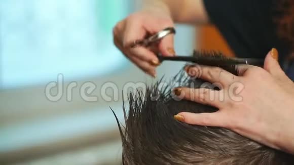 在美发沙龙剪小男孩头发的理发师的双手合拢视频的预览图