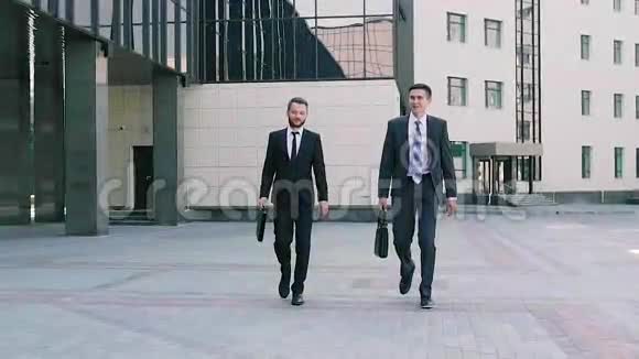 两个穿着智能西装的时髦商人走到办公室谈论即将到来的会议视频的预览图
