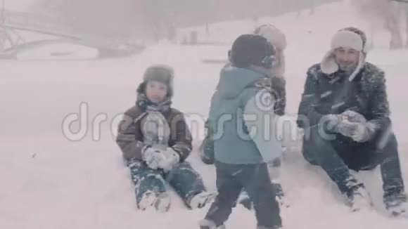 一家人坐在雪地上妈妈做雪球爸爸和一个孩子说话视频的预览图