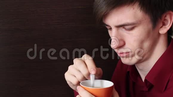 一个手里拿着一个橙色杯子的年轻人搅动着一茶匙看着杯子视频的预览图
