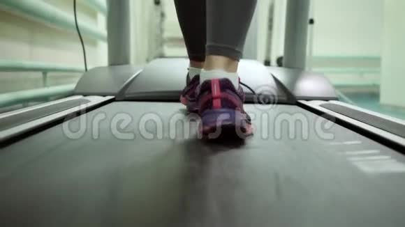 漂亮的白种人女孩在运动健身房的跑步机上跑步脚特写视频的预览图