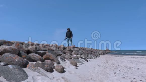 在海边的石墩上拿着相机的人视频的预览图
