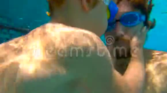 慢动作水下拍摄的父亲和他蹒跚学步的儿子在游泳池里游泳和玩耍视频的预览图