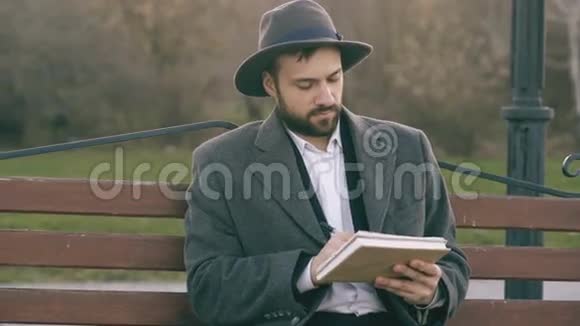 在公园里坐在城市街头的长椅上一个戴着帽子穿着外套拿着笔和素描的艺术家视频的预览图