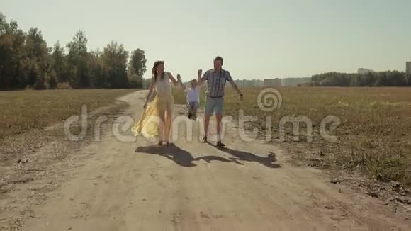 年轻的幸福家庭牵着手沿着乡间小路奔跑享受着阳光明媚的一天视频的预览图