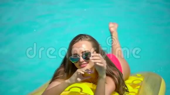 年轻女子20多岁在暑假在游泳池附近放松比基尼女孩日光浴躺在充气床上视频的预览图