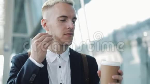 年轻有魅力的男人走在街上拿着咖啡听着耳机听着音乐走来走去视频的预览图