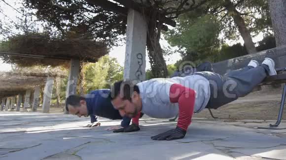 与户外私人教练一起健身两个健身男子做俯卧撑脚抬高在公园作为锻炼的一部分视频的预览图