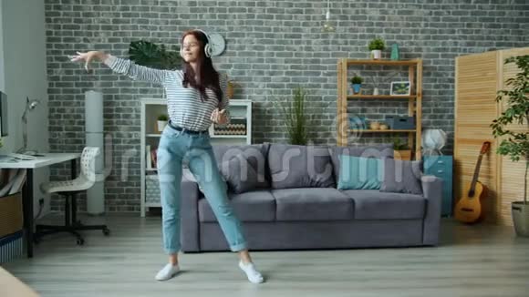 戴着耳机在公寓里跳舞的漂亮年轻女子独自在家享受乐趣视频的预览图