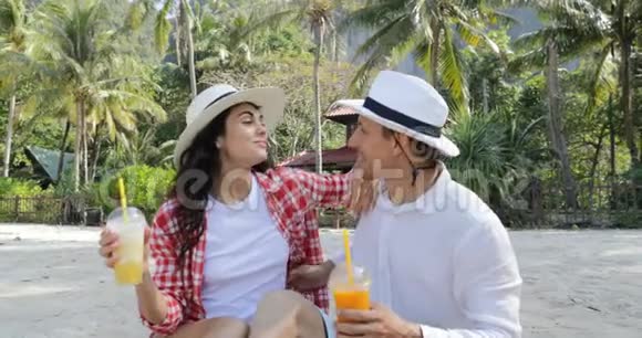 沙滩上的情侣谈酒汁谈坐棕榈树下的幸福男人和女人接吻视频的预览图