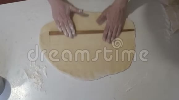 房子里的女人用木制的擀面杖在一张白色的桌子上把面团卷成一个圆圈形状视频的预览图