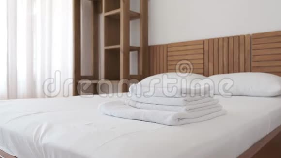 一套白色毛巾和毯子躺在酒店房间的舒适的床上上面有白色的窗帘视频的预览图
