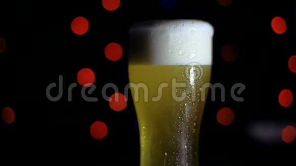 酒吧里有一杯黑色背景上的冷啤酒上面有彩灯啤酒在玻璃杯里起泡高清高清视频的预览图