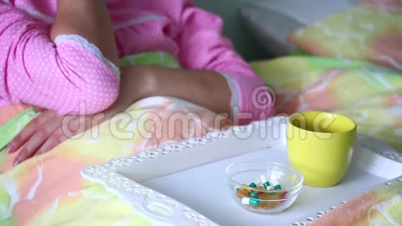 生病时一个女人躺在毯子下面取片用托盘处理一杯水饮用视频的预览图