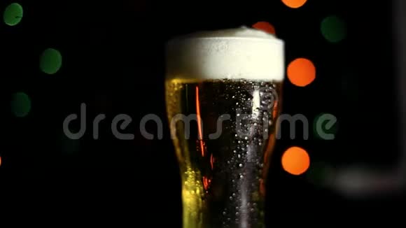 黑色背景上的一杯冷啤酒有彩灯水滴顺着玻璃流下来高清高清视频的预览图