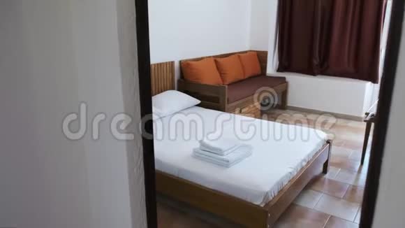 一间带白色双人床的酒店客房带橙色靠垫和巧克力窗帘的棕色沙发视频的预览图