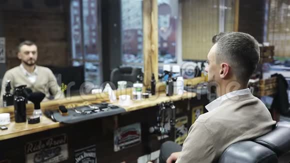 一个迷人的男人看着镜子在理发店里抚摸他的胡子视频的预览图