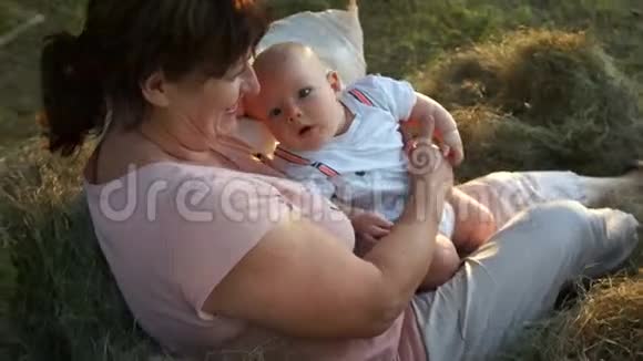 一位年轻的祖母把她的小孙子抱在怀里这孩子看上去很惊讶女人和婴儿坐在花园里视频的预览图