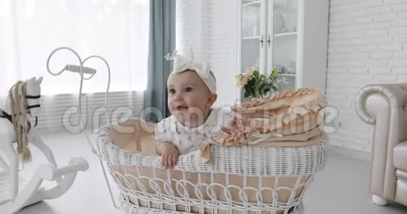 一个穿着裙子的可爱的小女孩坐在柳条白色婴儿车里环顾四周视频的预览图