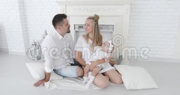 一对幸福的夫妇和一个小女儿坐在白色壁炉旁接吻视频的预览图