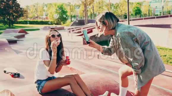 戴太阳镜的年轻女人吹泡泡玩得开心她的朋友打电话年轻的慢动作电影视频的预览图