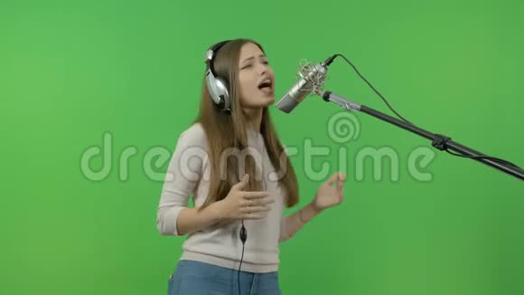 白姑娘有感情地唱进演播室的话筒里录制一段音乐片段在绿色背景下视频的预览图