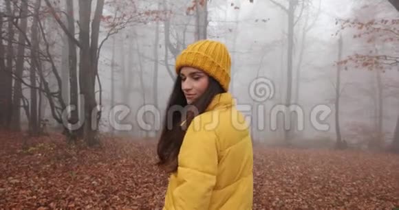 秋天的震动雾蒙蒙的森林漂亮的黑发女人长发穿着黄色的衣服穿过森林视频的预览图