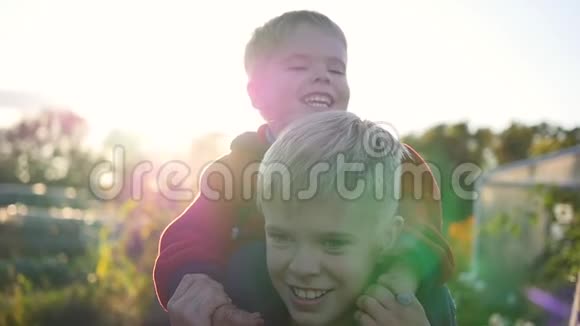 男孩拥抱他的弟弟把他抱在肩膀上孩子们欢声笑语日落视频的预览图