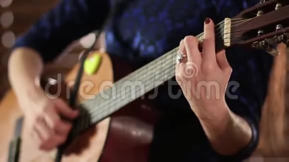 一个穿蓝色衣服的女孩在弹声吉他特写镜头手放在乐器的弦上离焦端o处视频的预览图